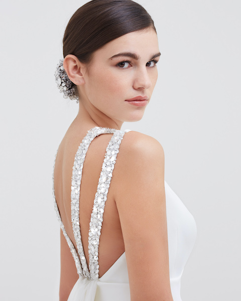 In questa foto una modella mostra il dettaglio sulla schiena di un abito da sposa: le bretelle sono tempestate di punti luce, proprio come il copri chignon