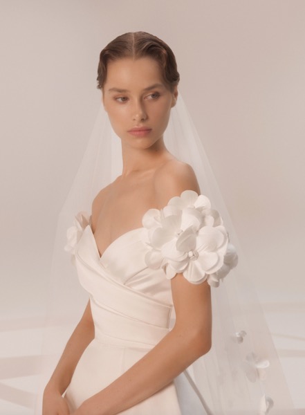 In questa foto una modella indossa un abito da sposa con fiori in mikado di seta 3D applicati sulle maniche