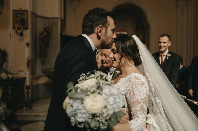 In questa foto i due sposi Pinuccia e Andrea mentre lei arriva all'altare e lui le da un bacio sulla fronte. In primo piano è presente il bouquet 