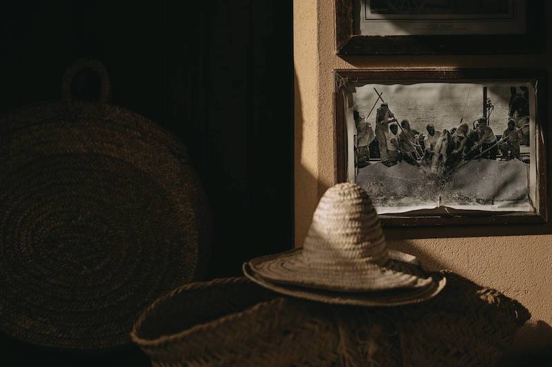 In questa foto un cappello di paglia a punta poggiato su una coffa tra antiche foto in bianco e nero