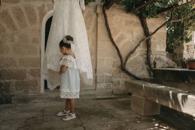 In questa foto la damigella del matrimonio di Pinuccia e Antonio con un vestitino colore azzurro polvere a pois bianchi e con bordi in pizzo chantilly tocca l'abito della sposa appeso a un tralcio di vite