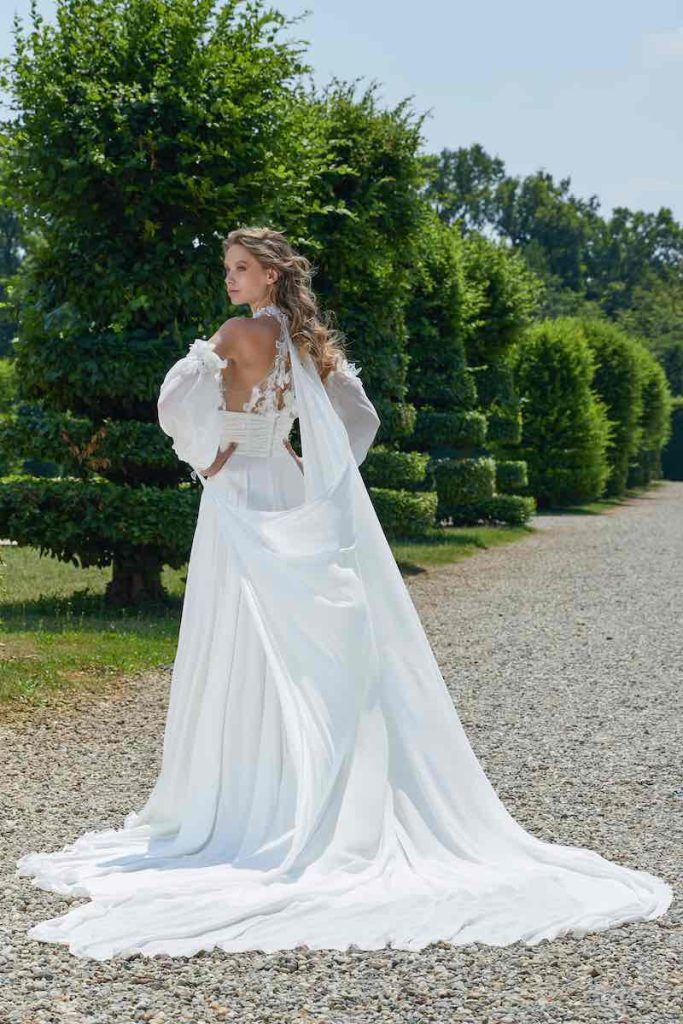 In questa foto una modella inquadrata di spalle indossa un abito da sposa scivolato in georgette con mantella legata alla nuca
