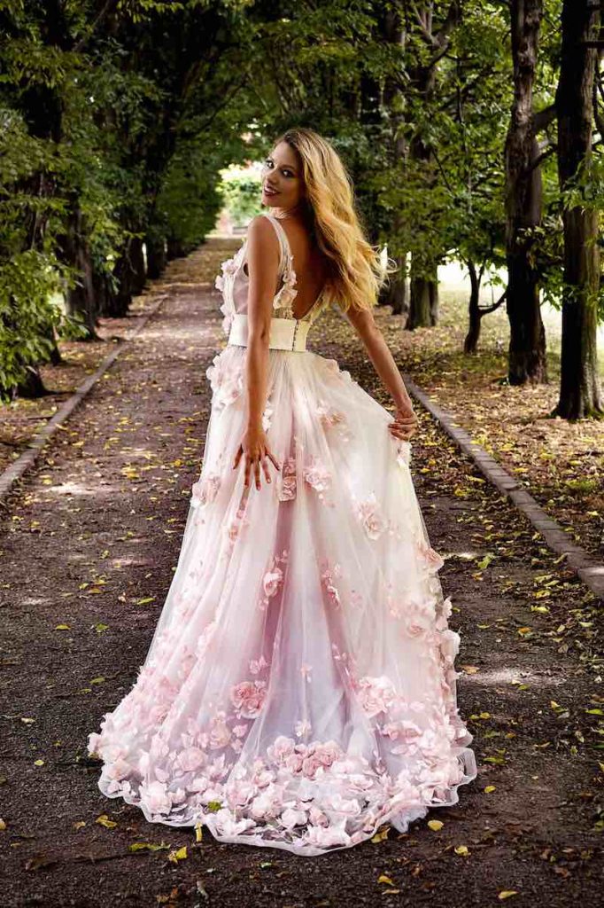 In questa foto una modella ritratta di spalle mentre corre indossa un abito da sposa colorato Stefano Blandaleone con rose 3D su tutta la lunghezza