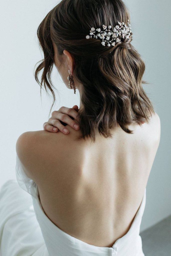 In questa foto una modella mostra un'acconciatura da sposa corta e mossa decorata con un fermaglio di cristalli e perline