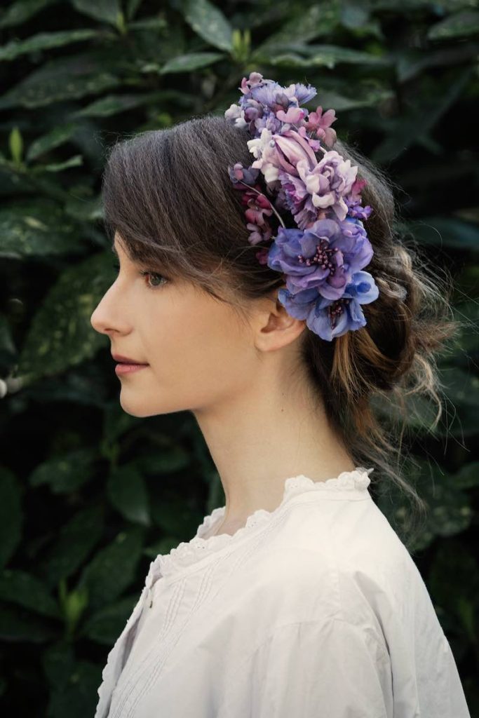 In questa foto una modella di profilo indossa un cerchietto con fiori di stoffa in varie tonalità di viola e lilla