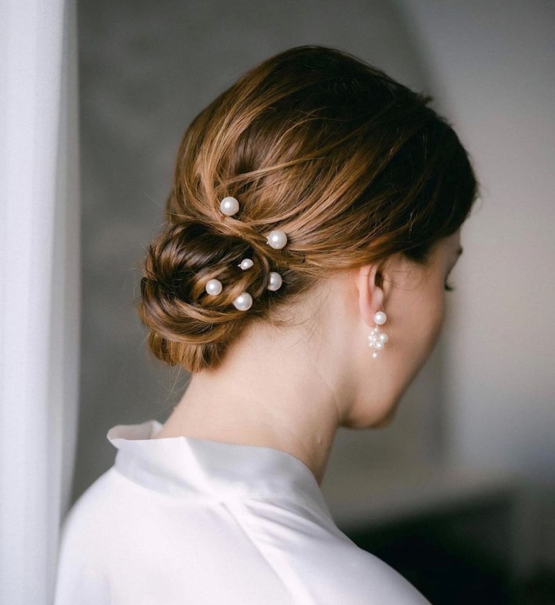 In questa foto una sposa di spalle mostra una delle acconciature sposa 2023: uno chignon basso con fermagli di perline