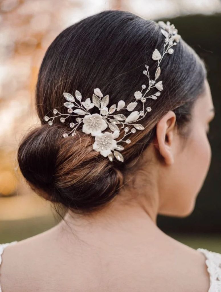 In questa foto una sposa di spalle mostra uno chignon basso decorato con un ramage gioiello di fiori e foglie