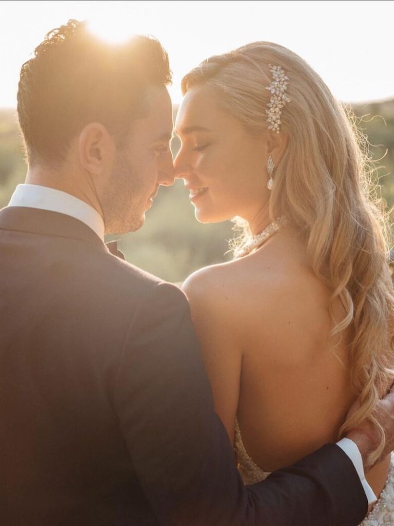 In questa foto due sposi si guardano al tramonto. La sposa porta i capelli lunghi sciolti e con onde morbide fermate da una spilla gioiello