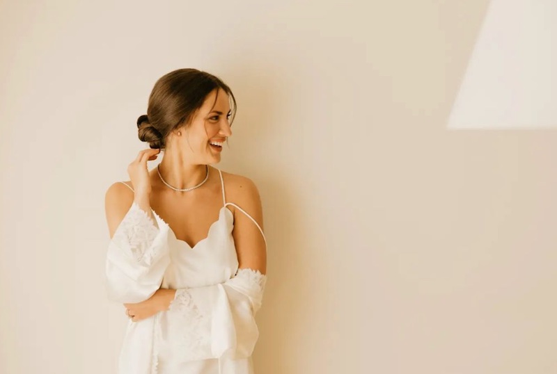 In questa foto una sposa ritratta davanti ad un muro ride e, di profilo, mostra uno chignon basso 