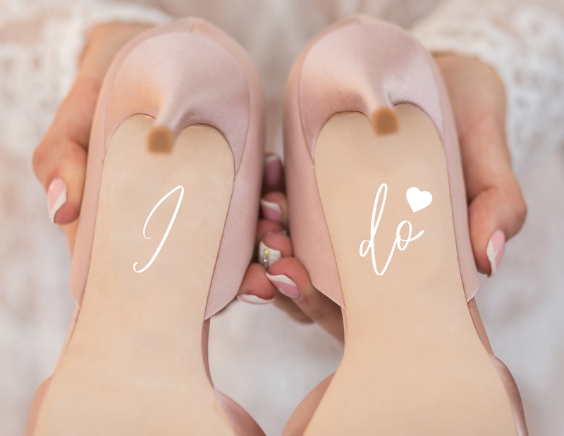 In questa foto il dettaglio della suola di un paio di scarpe da sposa di colore rosa decorate con stickers con la scritta I Do