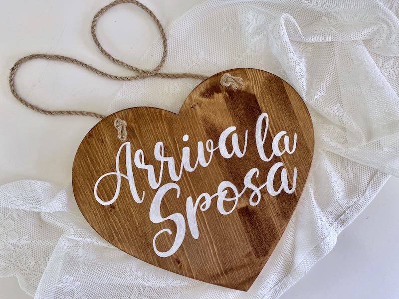 In questa foto un gadget matrimonio 2023 , cioè un cartello di legno a forma di cuore con scritto "Arriva la sposa"