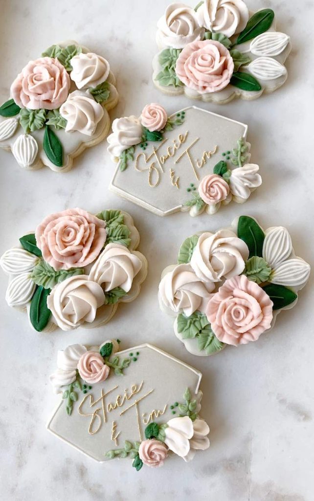 In questa foto biscottini personalizzati per matrimonio decorati con glassa con i nomi degli sposi e rose 3D di colore rosa e di colore bianco