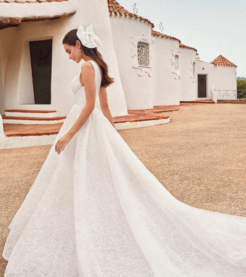 In questa foto una modella inquadrata di profilo indossa un abito da sposa ad A di Atelier Emé. Il look è completato da un maxi fiocco di colore bianco appuntato sulla nuca