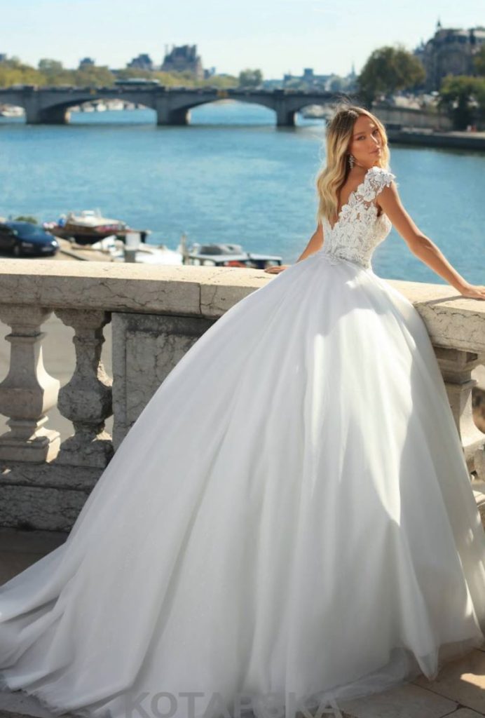 In questa foto una modella ritratta di spalle indossa un abito da sposa principessa Iryna Kotapska con corpetto in pizzo floreale con scollatura a V sulla schiena e gonna in mikado e tulle