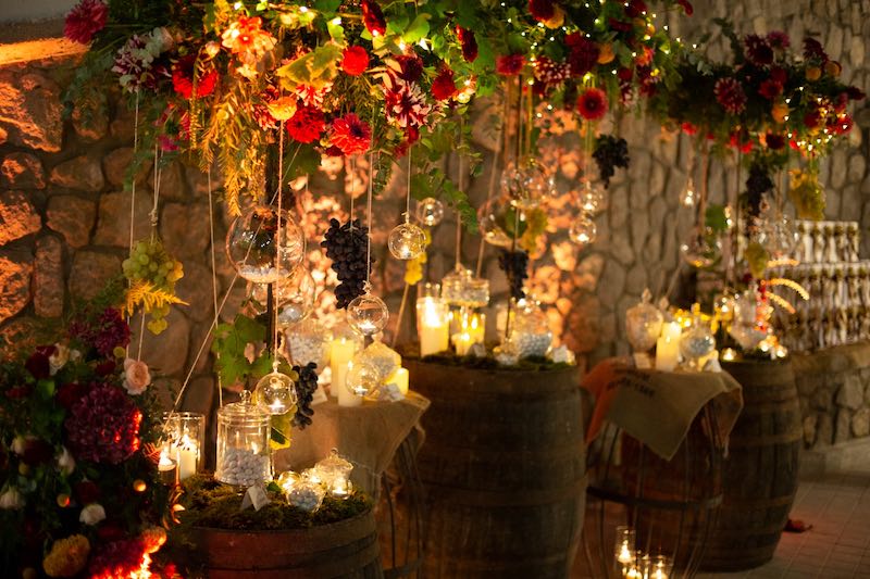In questa foto l'angolo dei dolci allestito dal Wedding Planner Stefano Miranda su botti di legno con decorazioni aeree di fiori di colore rosso e sfere di vetro illuminate da candele