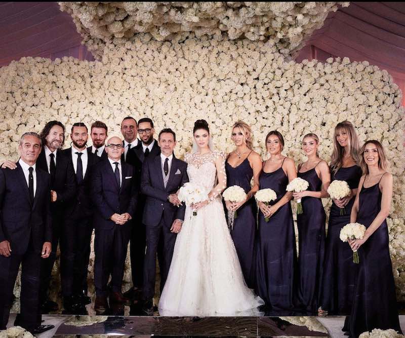 In questa foto Marc Anthony e Nadia Ferreira posano davanti a un wall di rose bianche con le damigelle in abito blu navy, i testimoni, Maluma e David Beckham