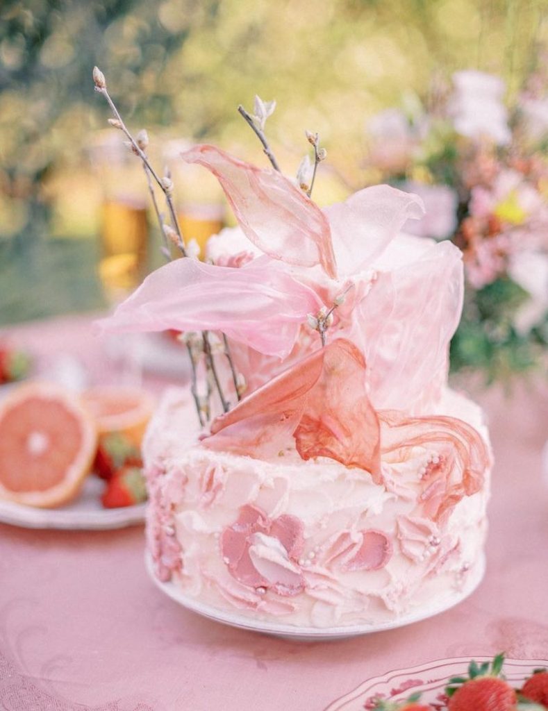 In questa foto una torta nuziale nei toni del rosa decorata con petali di zucchero e pennellate di crema 