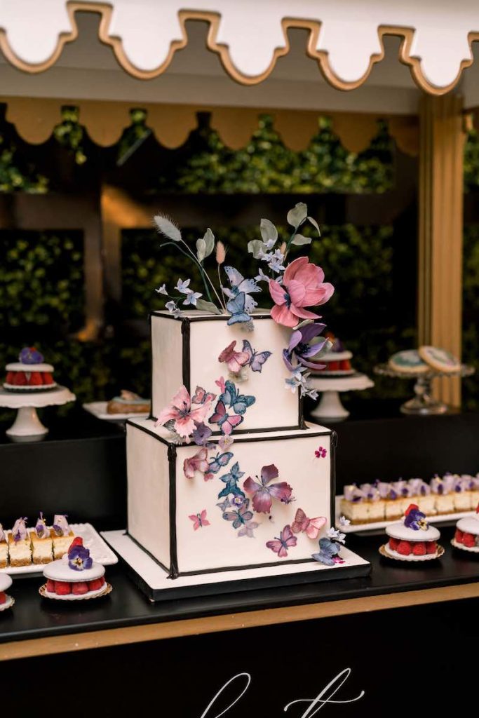 In questa foto una torta nuziale a piani di forma quadrata decorata con farfalle di colore rosa e azzurro
