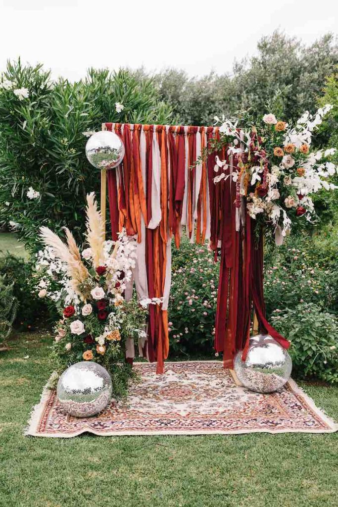 In questa foto un arco per matrimonio civile realizzato con composizioni floreali nei toni del rosa, del rosso e del bianco, nastri nei colori del Viva Magenta, del rosa e dell'arancione e palle strobo color silver