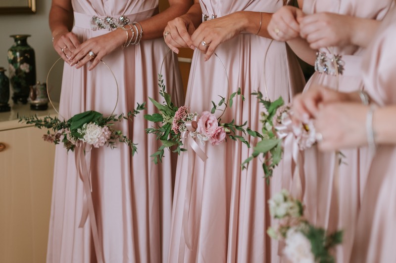 In questa foto il dettaglio di quattro damigelle con abiti di colore rosa che tengono in mano hoop bouquet con fiori di colore rosa 
