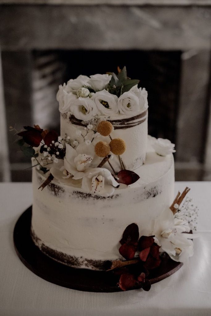 In questa foto una torta nuziale a due piani decorata con crema e fiori di colore bianco, rosso e giallo