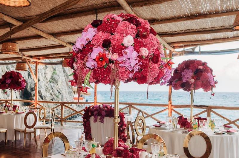 In questa foto un allestimento per matrimonio nei toni del rosa, del Viva Magenta e dell'oro composto da sedute e grandi composizioni floreali posizionate su centrotavola