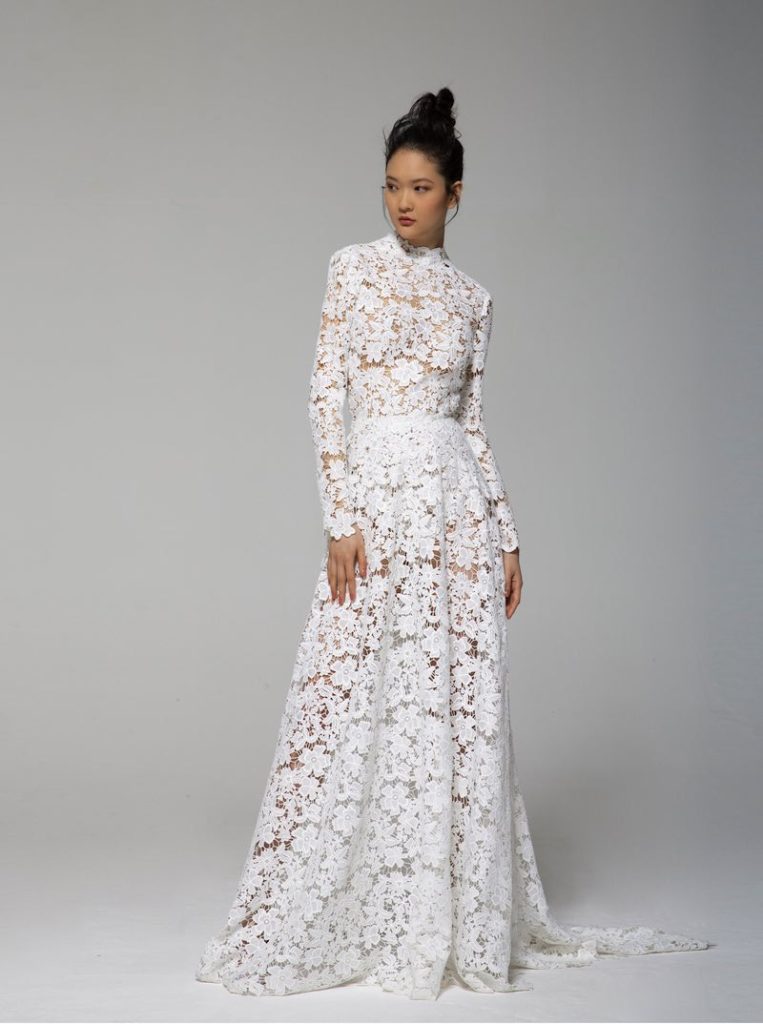 In questa foto una modella indossa un abito da sposa in pizzo macramè di Tosca Spose 2023 con girocollo e maniche lunghe