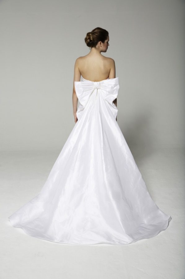 In questa foto una modella ritratta di spalle indossa un abito da sposa in taffetá con maxi fiocco che scende creando un ampio strascico