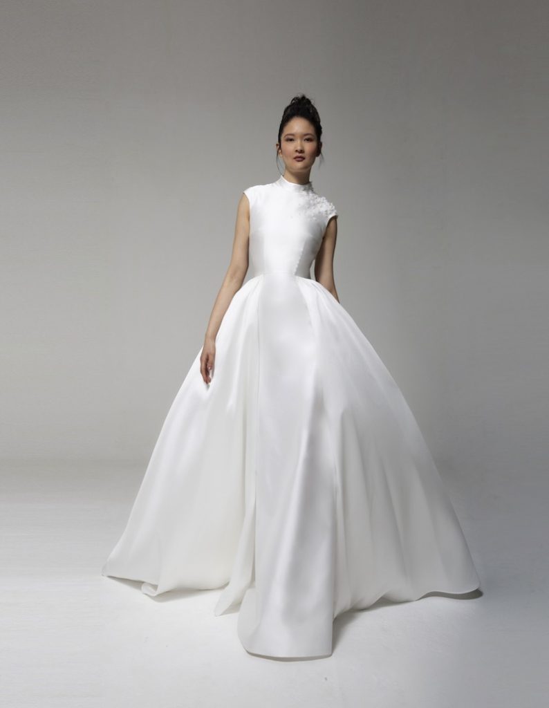 In questa foto una modella indossa l'abito Tosca Spose 2023 "L'onda" in mikado di seta liscio con collo alto e maniche corte