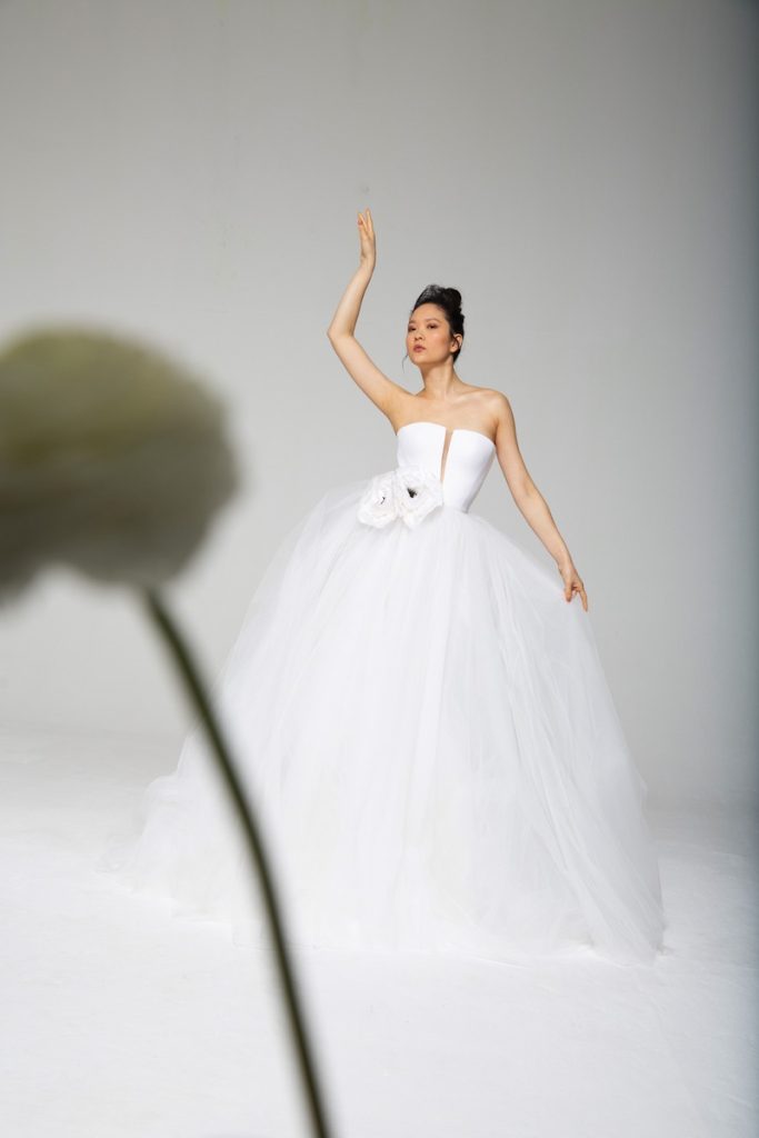 In questa foto una modella indossa l'abito Tosca Spose 2023 le "Ballerine" con gonna in tulle, corpetto in mikado senza spalline con scollo a V e due fiori maxi in vita