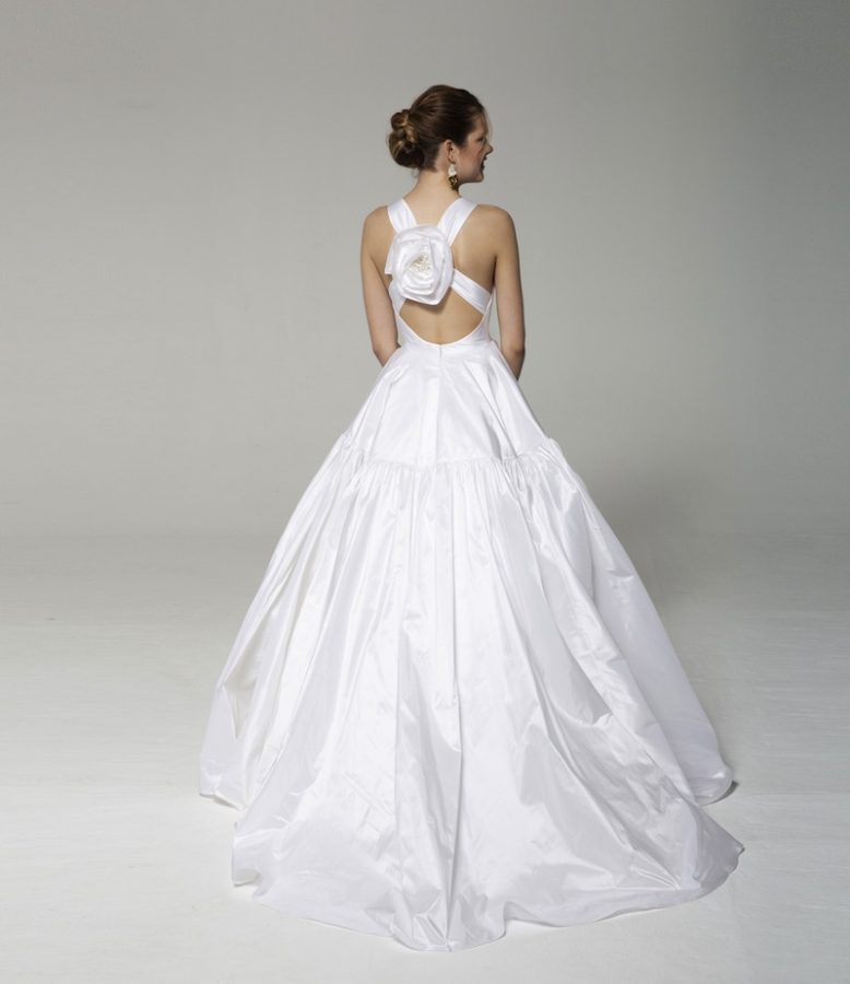 In questa foto una modella ritratta di spalle indossa l'abito Tosca Spose 2023 "Ritratto" in taffetá con incrocio sulla schiena e maxi fiore  