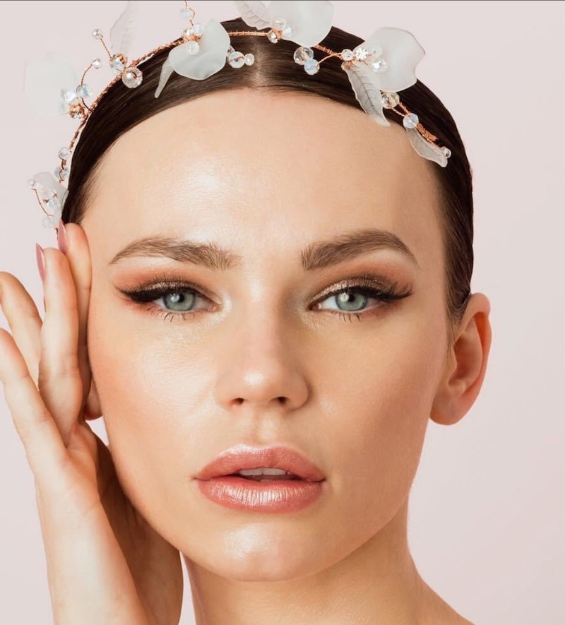 In questa foto una modella posa mostrando un trucco sposa illuminante 2023 con rossetto rosato satinato e riga di eyeliner