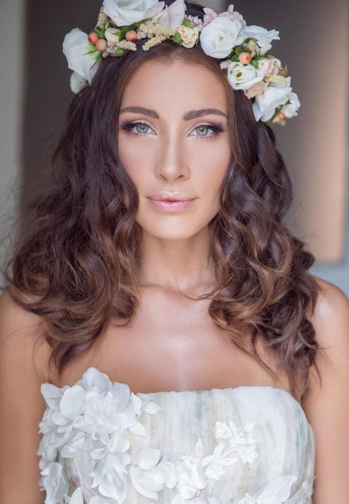 In questa foto una modella posa mostrano un trucco sposa romantico e indossa una coroncina di fiori su capelli sciolti e mossi