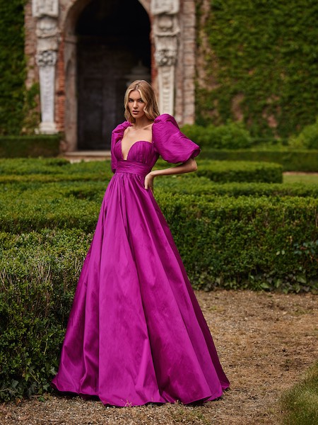 In questa foto una modella indossa un bellissimo abito con gonna ampia e maniche balloon in color magenta. Fa parte della collezione di vestiti da cerimonia Nicole Milano 2023