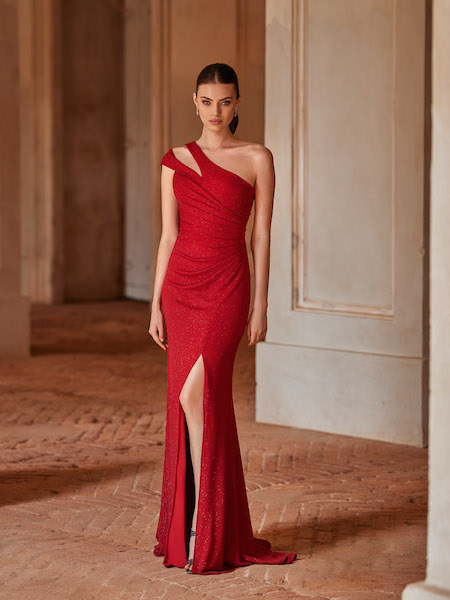 In questa foto una modella indossa un abito da cerimonia 2023 rosso, a sirena monospalla e con piccolo spacco sulla coscia