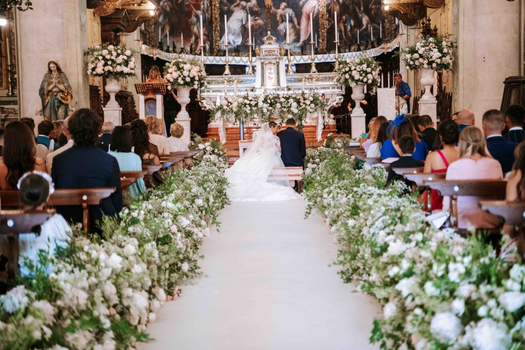 In questa immagine un allestimento floreale matrimonio 2023 di una chiesa con tantissimi fiori bianchi ai bordi della navata.