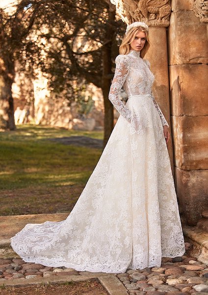 In questa foto una modella indossa un abito da sposa Pronovias 2023, della capsule Essence of Love, interamente ricamato in pizzo, con collo alto e maniche lunghe