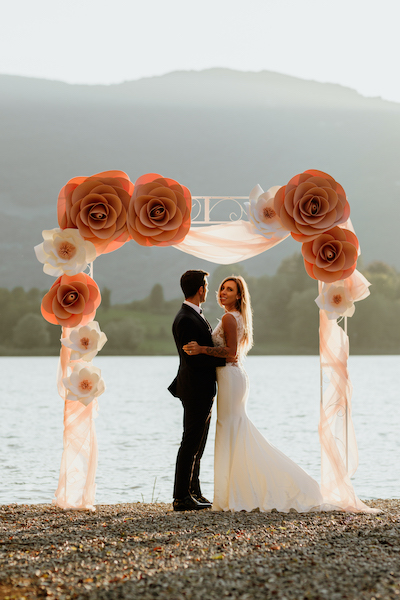 In questa foto due sposi con alle spalle un arco fatto con i fiori di carta gigante di Incartesimi, una delle idee per le nozze più sofisticate