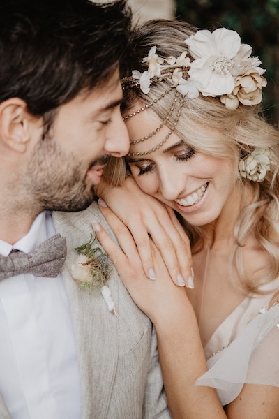 In questa foto una sposa appoggia la sua testa sulla spalla del marito, mentre indossa un fascinator con fiori in tessuto realizzato da OfficineLamour