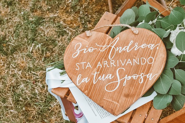 In questa foto una targa di legno, realizzata da Where Pretty Happens, a forma di cuore con su scritto Zio Andrea, sta arrivando la tua sposa