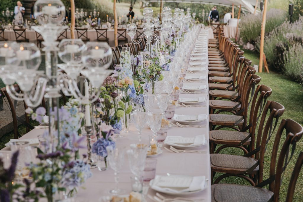 In questa immagine, una mise en place con candele e vasetti colmi di fiori. 