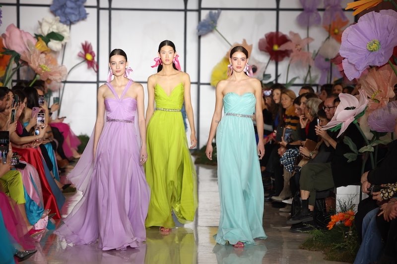 In questa foto tre modelle sfilato in passerella a Milano indossando tre abiti da cerimonia Atelier Emé 2023 dalla linea scivolata di colore lilla, verde lime, verde acqua
