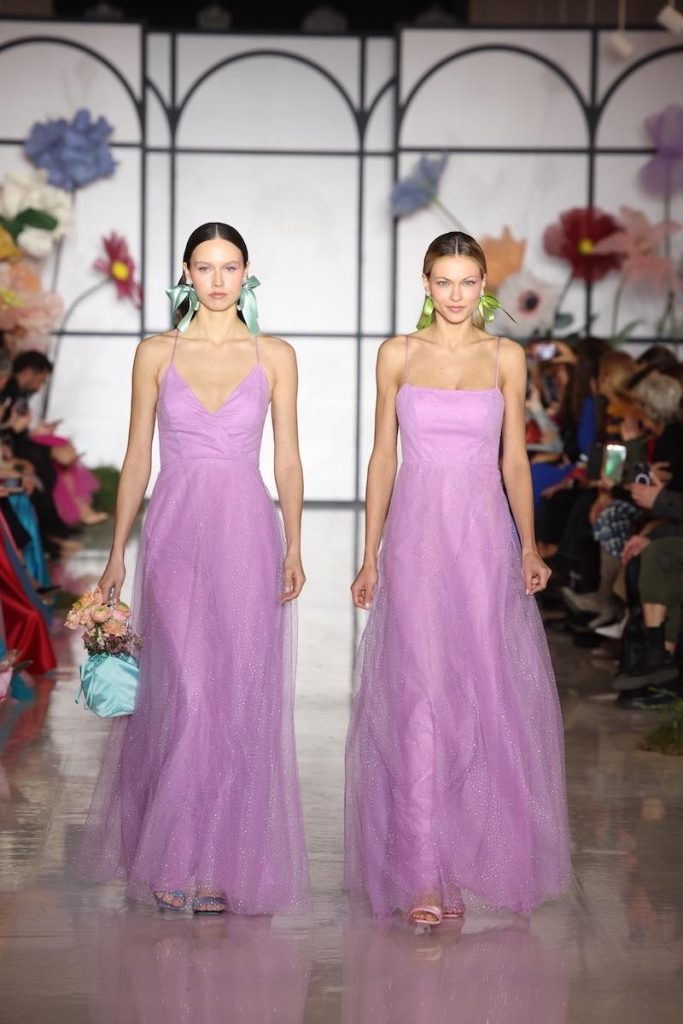 In questa foto due modelle sfilano con due abiti da cerimonia Atelier Emé 2023 di colore lilla con gonna in tulle sparkling