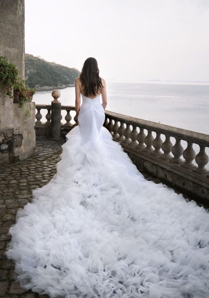 In questa foto una modella indossa un abito da sposa Dovita Bridal 2023 a sirena con lungo strascico di ruches di tulle