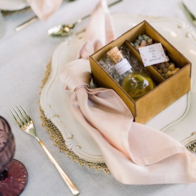 In questa foto una bomboniera di matrimonio con olio aromatizzato in scatola poggiata su un piatto di porcellana