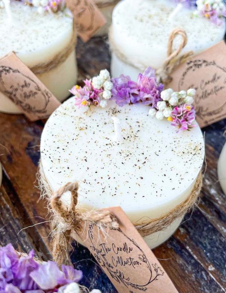 In questa foto candele con fiori essiccati di colore lilla e bianco e un nastro di juta usate come bomboniere per matrimonio 2023