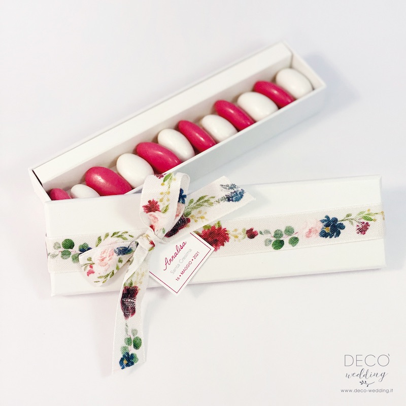 In questa foto una scatolina per confetti di froma rettangolare con nastro fiorato e confetti di colore bianco e rosso