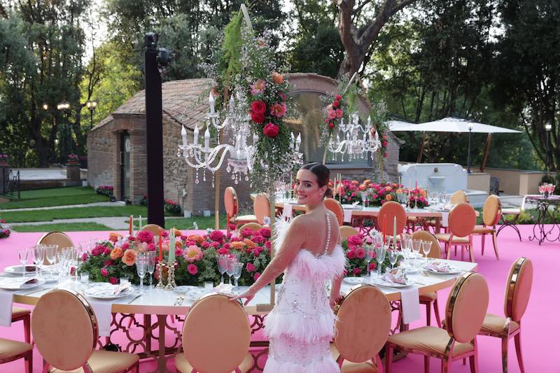 In questa foto la sposa Alexandra posa di spalle, con la testa rivolta verso l'obiettivo nella location del ricevimento allestita nei toni dell'oro, del fucsia e dell'arancione