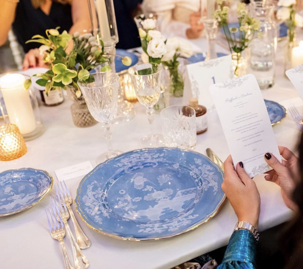 In questa immagine, una mise en place matrimonio 2023 con piatto blu e bordo in oro, posate silver e bicchieri in cristallo.