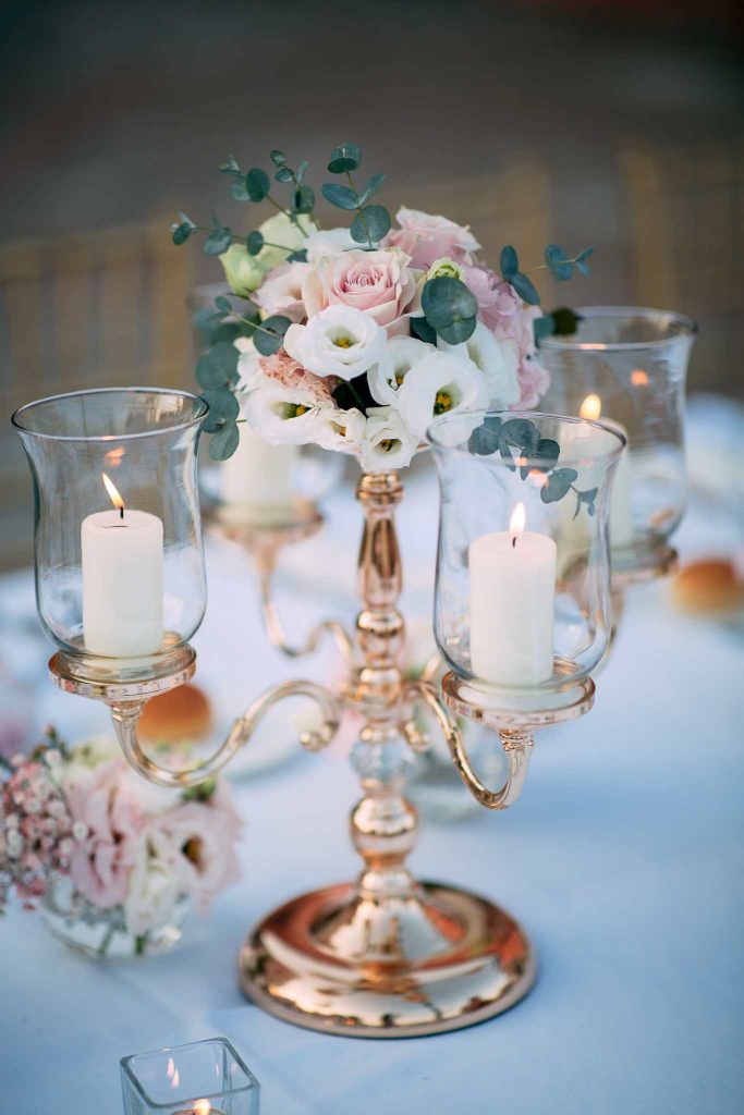 In questa immagine una delle tendenze delle mise en place 2023 con candelabri con candele e vasetti di fiori freschi. 